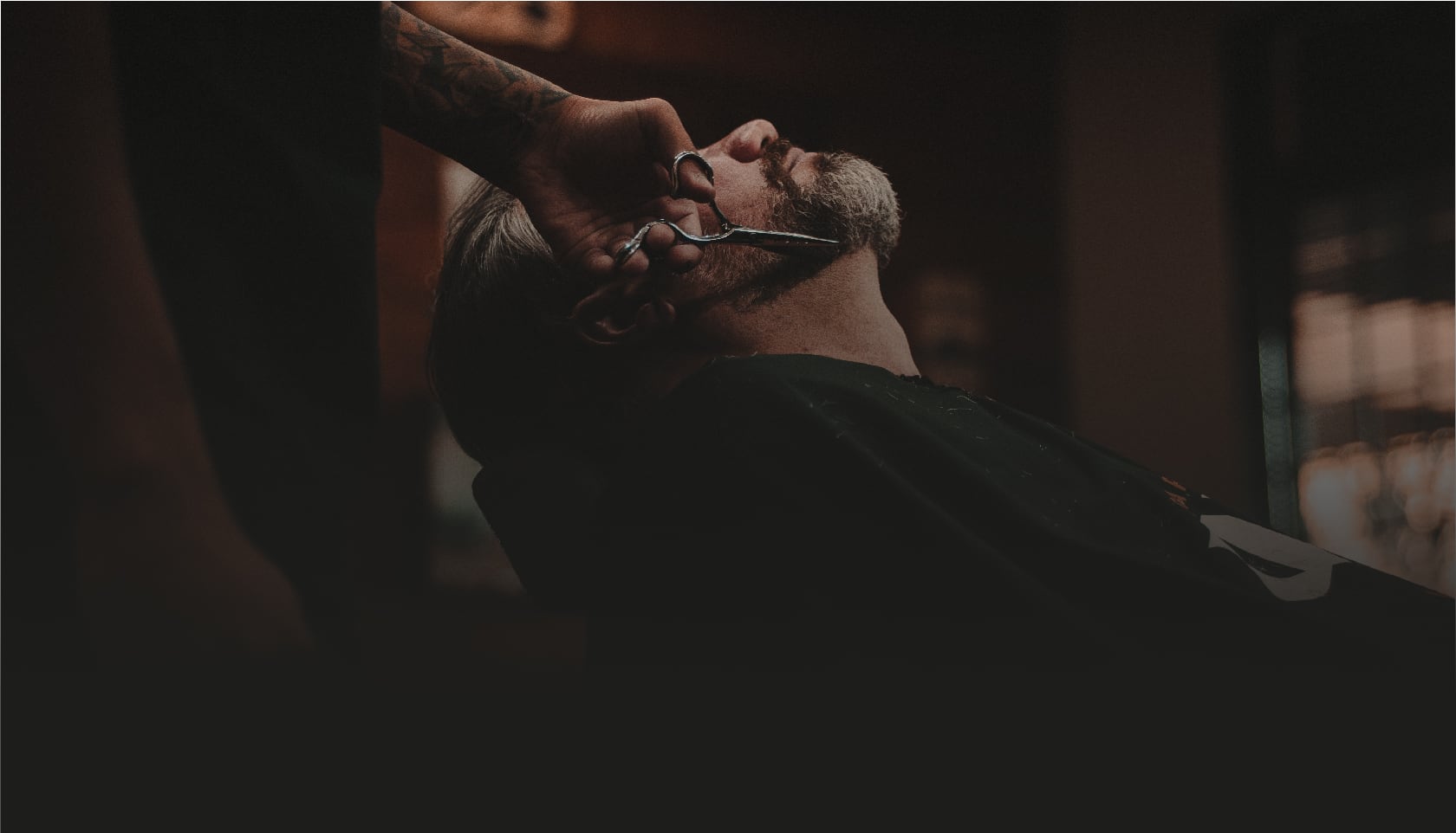 Barbier die met een schaar de baard van een klant bijknipt in een sfeervolle, warm verlichte barbershop